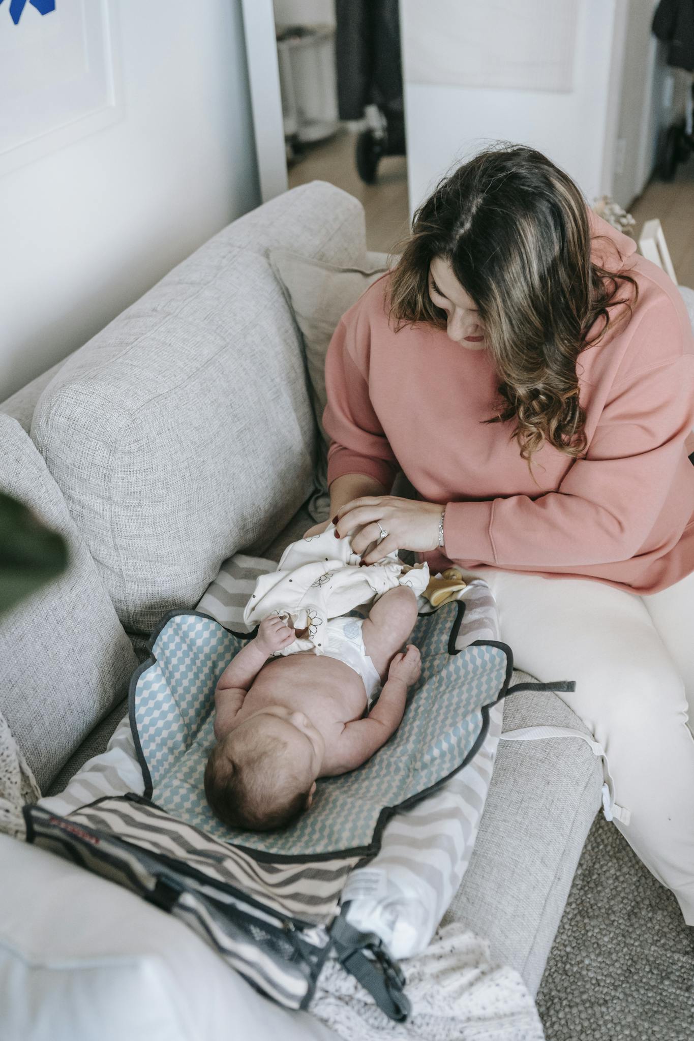 A serene moment of a mother changing her baby's diaper on a sofa at home.
