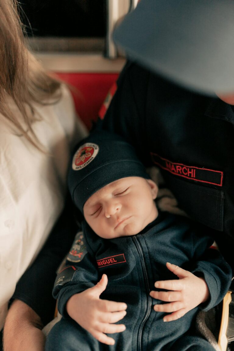 Adorable baby asleep in firefighter attire, embraced by parents.