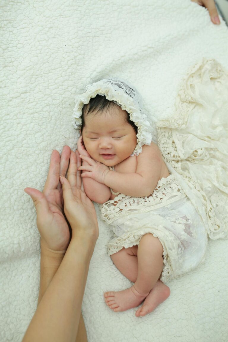 Charming newborn baby in lace bonnet and wrap sleeping peacefully, supported gently by adult hands.