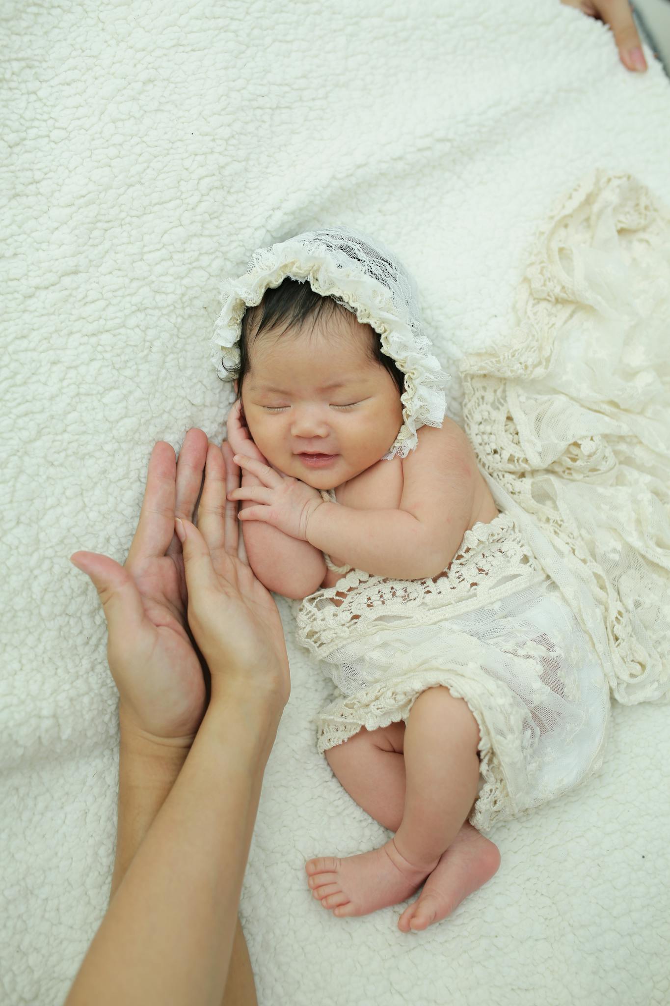 Charming newborn baby in lace bonnet and wrap sleeping peacefully, supported gently by adult hands.