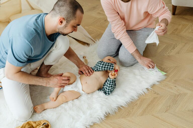 Two fathers changing their baby's diaper on a soft white rug at home, demonstrating parenting and togetherness.